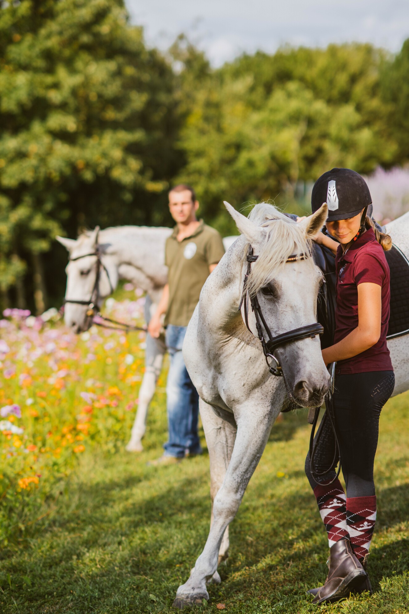 Hotel Reiters Finest Family - a girl and a man stand in the meadow with two saddled Lipizzaners